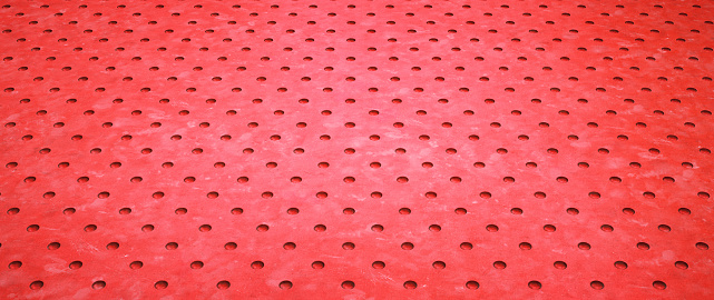 Extreme close-up on a red painted surface floor background with drilled holes and diminishing perspective. Wide horizontal composition.