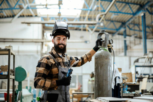 un trabajador con una máscara protectora en la cabeza se está preparando para hacer algunos trabajos de soldadura en su taller. trabajador con una máquina de soldar. - soldar fotografías e imágenes de stock