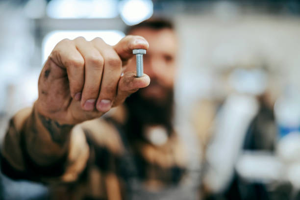 nahaufnahme der arbeiterhalteschraube. selektiver fokus auf finger mit einer schraube. werkzeug des arbeiters. arbeiter im geschäft - screw industry bolt nut stock-fotos und bilder