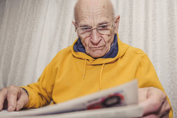 istock Aged grandpa with wrinkled face reading newspaper sitting at table 1341915902