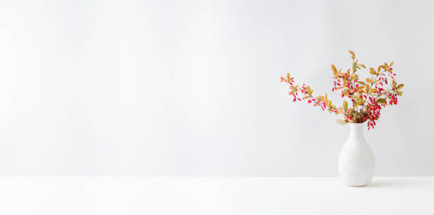 istock Home interior with decor elements. Colorful autumn leaves and red berries in a vase on a light background 1341922711