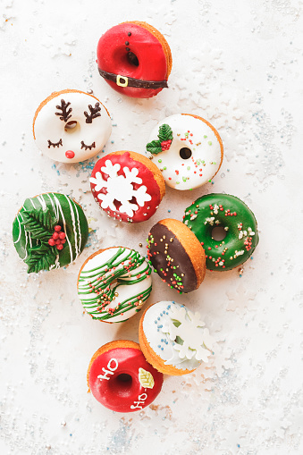 Christmas donuts. Assorted homemade glazed donuts with sprinkles on white festive background. Top view, blank space
