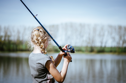 little blond child fishing fishes with fishing stick in natural pond
