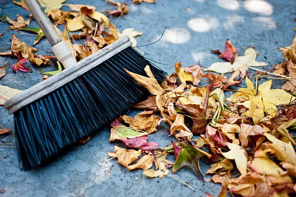 A broom is sweeping up a pile of colorful autumn leaves.