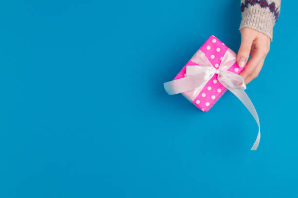 istock Small gift box in female hands on blue background, view from above 1341928482