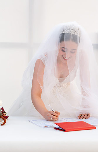 Young girl wearing a wedding dress signs the marriage certificate at the wedding table.