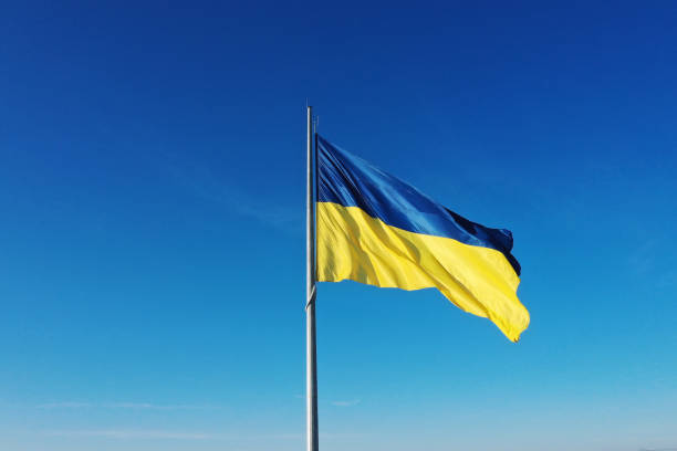 The flag of Ukraine develops on a flagpole against a background of clear sky stock photo