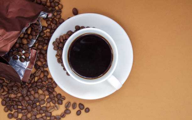 белая чашка черного кофе американо без молока с пучком обжаренных кофейных зерен, разбросанных по бумажной упаковке. фон кофе, вид сверху с  - coffee plant стоковые фото и изображения