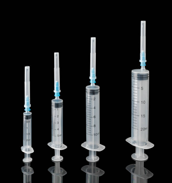 istock Four disposable syringes with sealed needles on a black background with reflection 1341934099