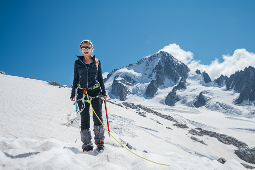 Happy cheerful sincerely laughing young female portrait in climbing harness, crampons, sunglasses, mountain team rope while she descending after successful mountain climbing. Happy active people image