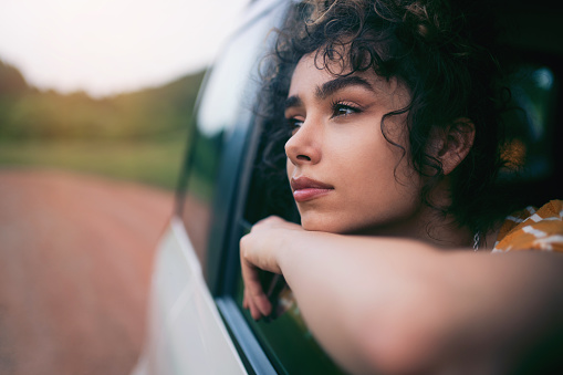 Beautiful young Caucasian woman with curly hair enjoying a road trip and looking out of the car window.