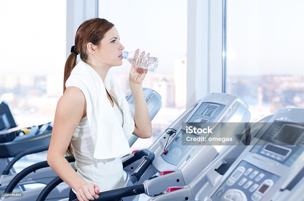 Young woman at the gym exercising. Drink Young woman at the gym exercising. Run on on a machine and drink water Activity Stock Photo