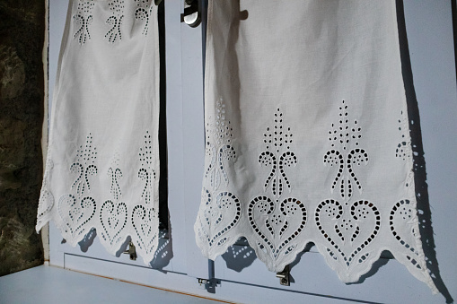 Blue window with white curtains with nice fabric decorated in hearts pattern close-up in house interior at night. Traditional Mediterranean house