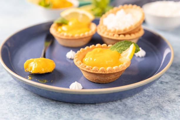 istock Lemon curd mini tarts decorated with mint and lemon slices on blue ceramic plate. 1341946820