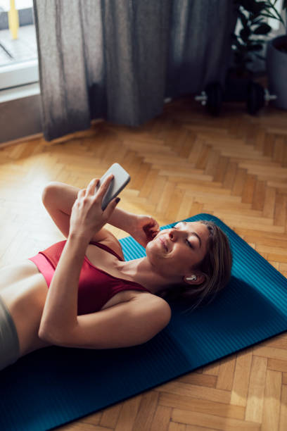 istock Smiling Woman With Wireless Earphones Lying On Exercise Mat and Using her Mobile Phone Before Workout 1341947305
