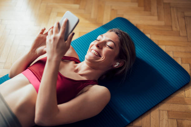 istock Smiling Woman With Wireless Earphones Lying On Exercise Mat and Using her Mobile Phone Before Workout 1341947315