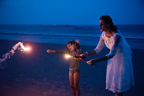istock Mature bride lighting bengal fire with daughter on the beach at dusk. 1341949935