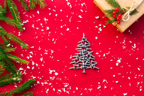 Christmas tree of screws, gift with branches of a Christmas tree and berries on a red background. Flat lay. Copy space. stock photo