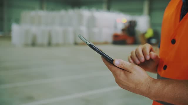 agriculture storage. warehouse. close-up. man's hands with tablet. an enterprise employee works on tablet against background of loading of corn seeds or sunflower grains bags at warehouse