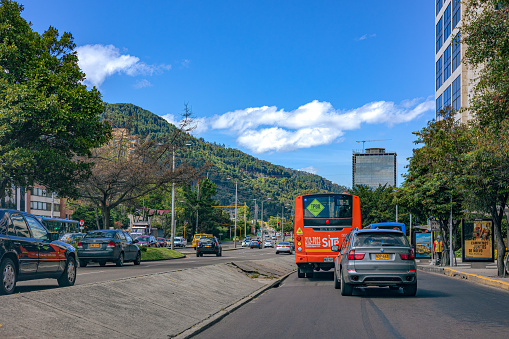 Bogotá, Colombia - September 18, 2021: The drivers point of view on Carrera Septima just approaching downtown Usaquén in the Andean capital city of Bogota, in South America. Most buildings in view are office buildings. Given the amount of rainfall Bogota receives annually, there are healthy trees everywhere. In the far background are the Andes Mountains. The altitude at street level is 8,660 feet above mean sea level. Horizontal format. Copy space.