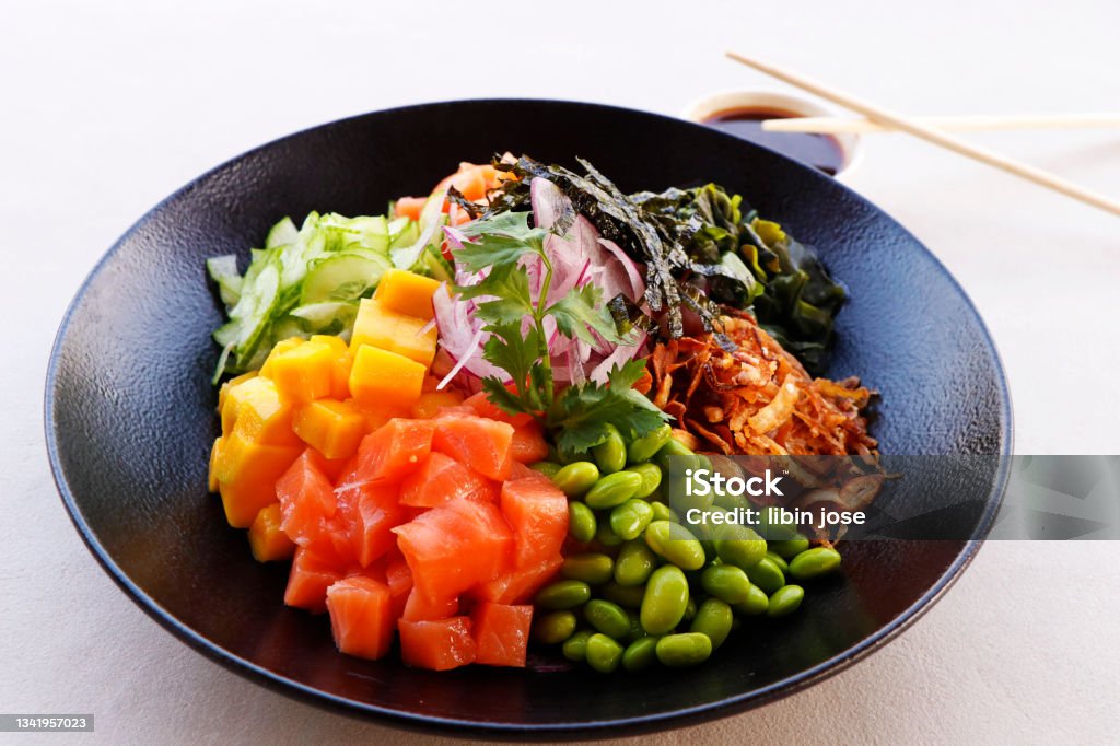 healthy poke bowl with edamame, salmon, wakame seaweed, mango, radish, cucumber, onion and rice served with sweet soy sauce, japanese food speciality Appetizer Stock Photo