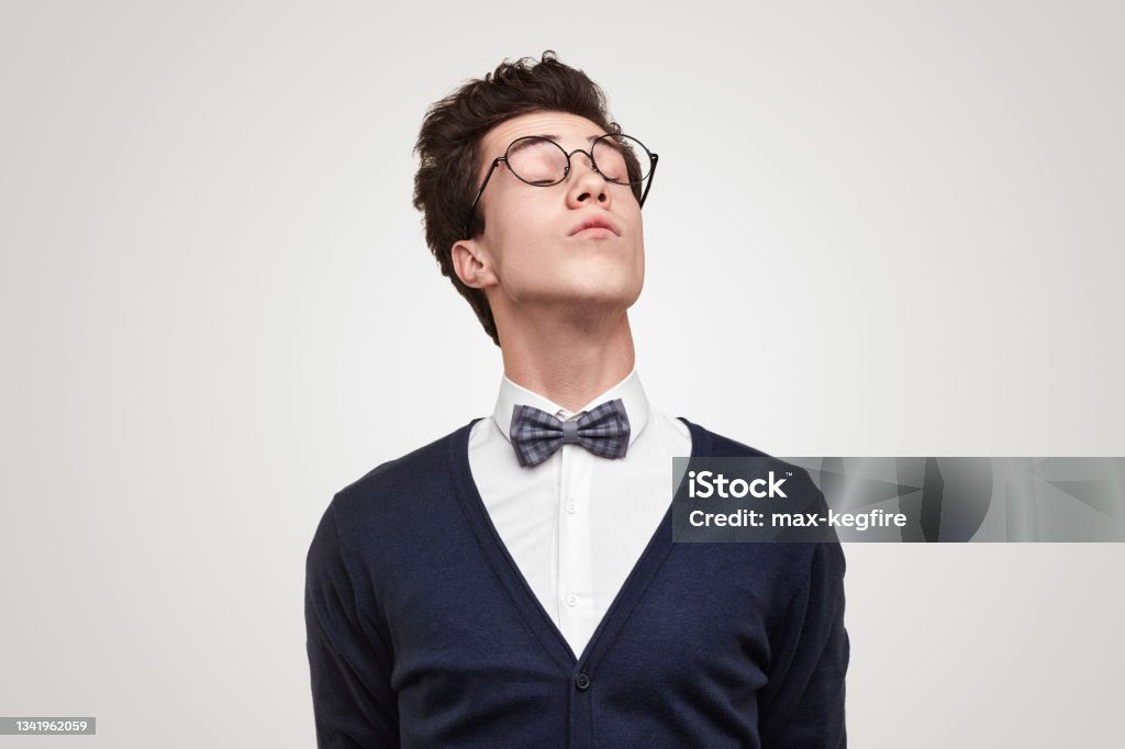 Haughty nerd with closed eyes Snobbish young man in glasses closing eyes and raising head against gray background Snob Stock Photo