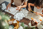 Little cute girl and young beautiful woman cut snowflakes from white paper. Gingerbread and cocoa with marshmallows