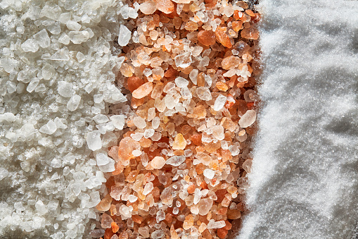 Top view of variety of salt:  Himalayan pink salt, coarse grain sea salt and white salt as background.