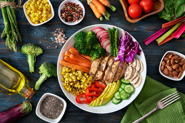 Healthy eating and diet concepts. Top view of spring salad shot from above on rustic wood table. Healthy eating and diet concepts. Colorful spring salad on rustic white wood table. Included ingredients: Chicken, tomatoes, broccoli, lettuce, bell peppers, mushroom, carrots, radicchio, almonds. healthy eating stock pictures, royalty-free photos & images