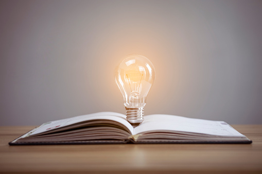Education knowledge and business studying concept, Closeup glowing light bulb and book on table background
