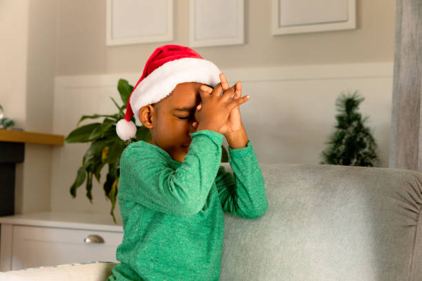 garçon afro-américain portant un chapeau de père noël et priant à noël - praying joy indoors lifestyles photos et images de collection