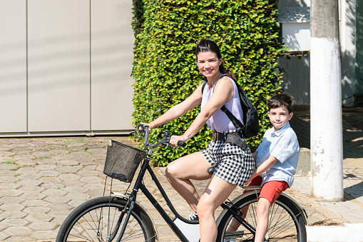 Mother (40 years old) and son (8 years old) riding a bike on a sunny morning in Brazil.