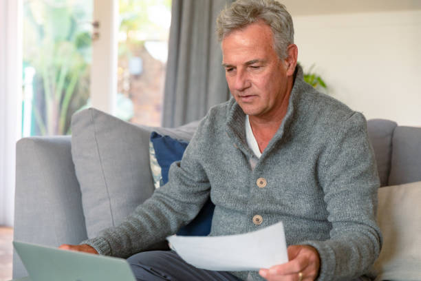 istock Focused caucasian senior man sitting on sofa, doing paperwork, using laptop 1341986980