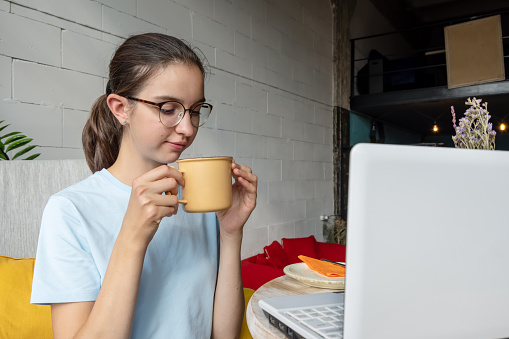 Beautiful girl student drinking coffee, tea, cocoa from a mug while sitting in front of a laptop. Business concept. Freelance concept