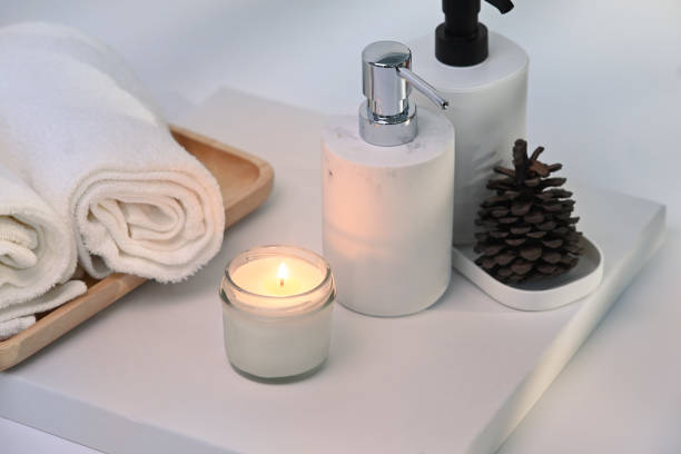 Burning wax candle, towels and shampoo bottles on white table.
