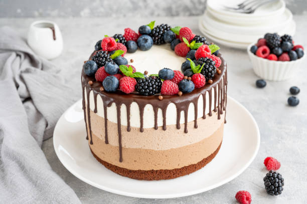 istock Three chocolate mousse cake with chocolate glaze, blueberries, raspberries and blackberries on top on a white plate on a gray concrete background. Cake with three layers of different taste. Copy space. 1341996776