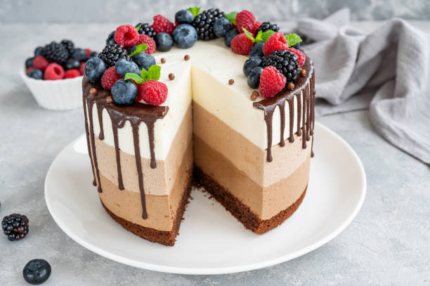 istock Three chocolate mousse cake with chocolate glaze, blueberries, raspberries and blackberries on top on a white plate on a gray concrete background. Cake with three layers of different taste. Copy space. 1341996785