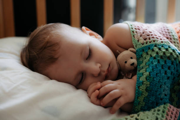 Cute baby sleeps peacefully in crib with handle under his cheek