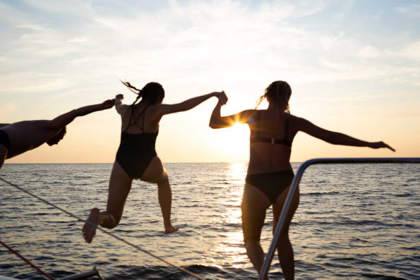 un grupo de amigos saltando al mar desde un yate al atardecer - child jumping swimming nautical vessel fotografías e imágenes de stock