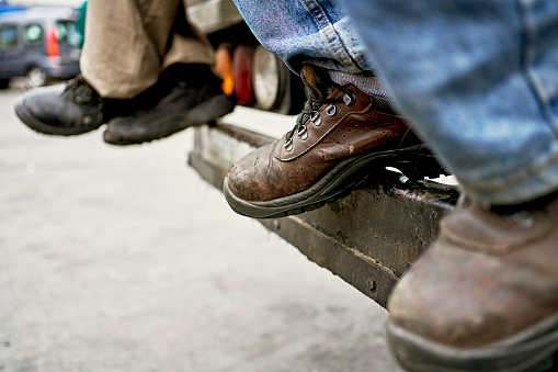 Close-up of male and female transportation worker shoes as they relax on back of delivery truck before departing on road trip.