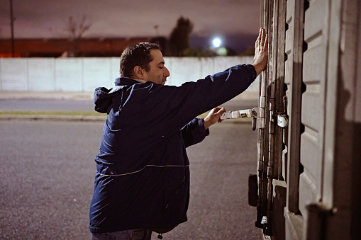 Waist-up side view of late 40s Hispanic man securing cargo door before starting on nighttime road trip.