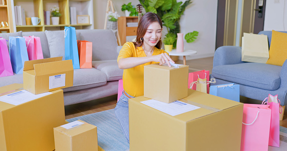 happy asian woman receive packing parcel after online shopping and opening a delivery box in the living room at home