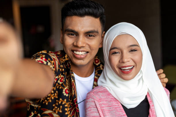 happy young Muslim couple taking selfie together at home Happy Young Muslim Woman In Hijab Taking Selfie Together with boyfriend, Cheerful Islamic Couple Posing And Smiling At Camera, Standing Together Over Gray Studio Background, Closeup Shot malay couple stock pictures, royalty-free photos & images
