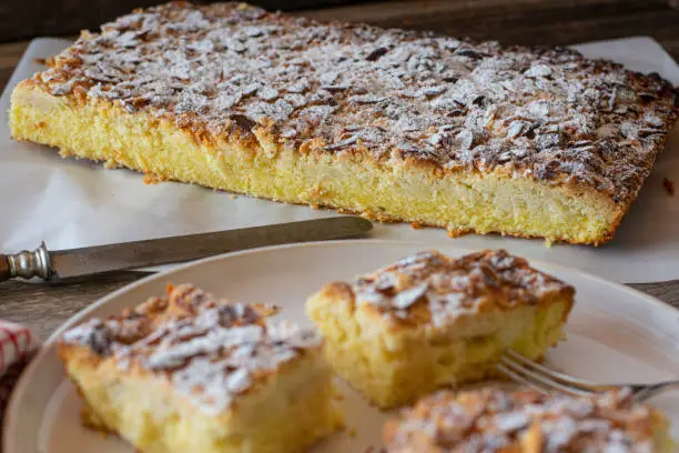 Homemade fresh baked, rustic sheet cake with crumble and almond topping. Served ready to eat on wooden table. Closeup view. Focus on background