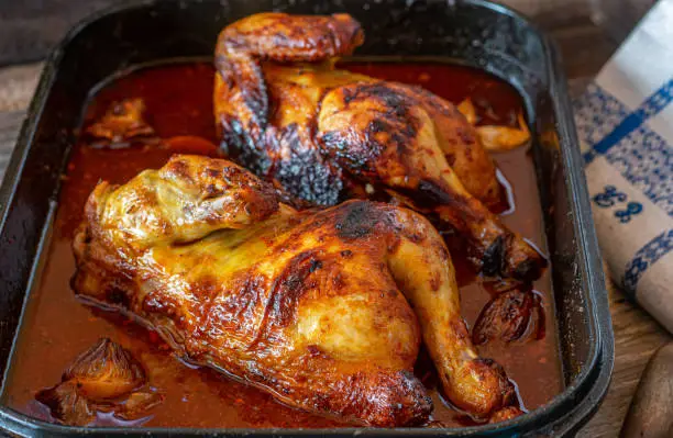 Delicious homemade marinated chicken with honey, garlic, paprika sauce served hot  in a baking dish on wooden table. Closeup