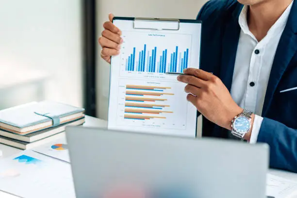 Photo of Business man is checking and auditing the business performance with a help from his college. Analyzing the revenue and auditing the budget concept.