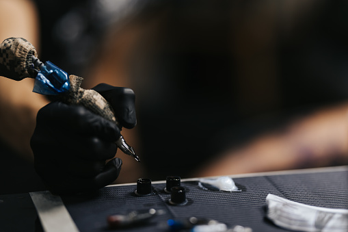 Tattoo master dips a tattoo machine with needles in black ink, close-up shot, unrecognizable person