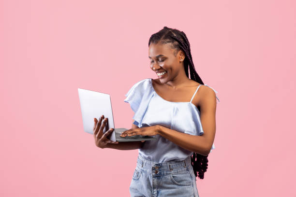 istock Young black woman with afro bunches using laptop, freelancing, browsing web on pink studio background 1342027323