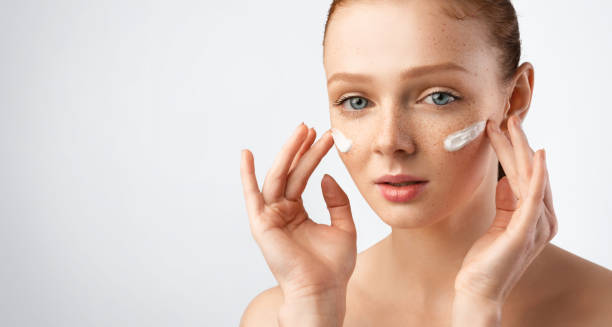 istock Young Woman Applying Moisturizer Cream On Cheeks Over Gray Background 1342027815