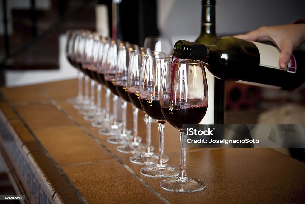 Mano vertiendo una Hilera de copas de vino para probar - Foto de stock de Vino libre de derechos